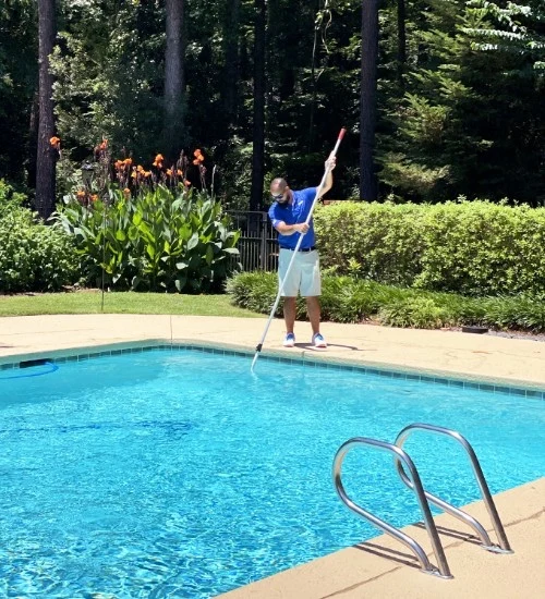 Splash Brothers technician cleaning a clear backyard pool with a pole brush
